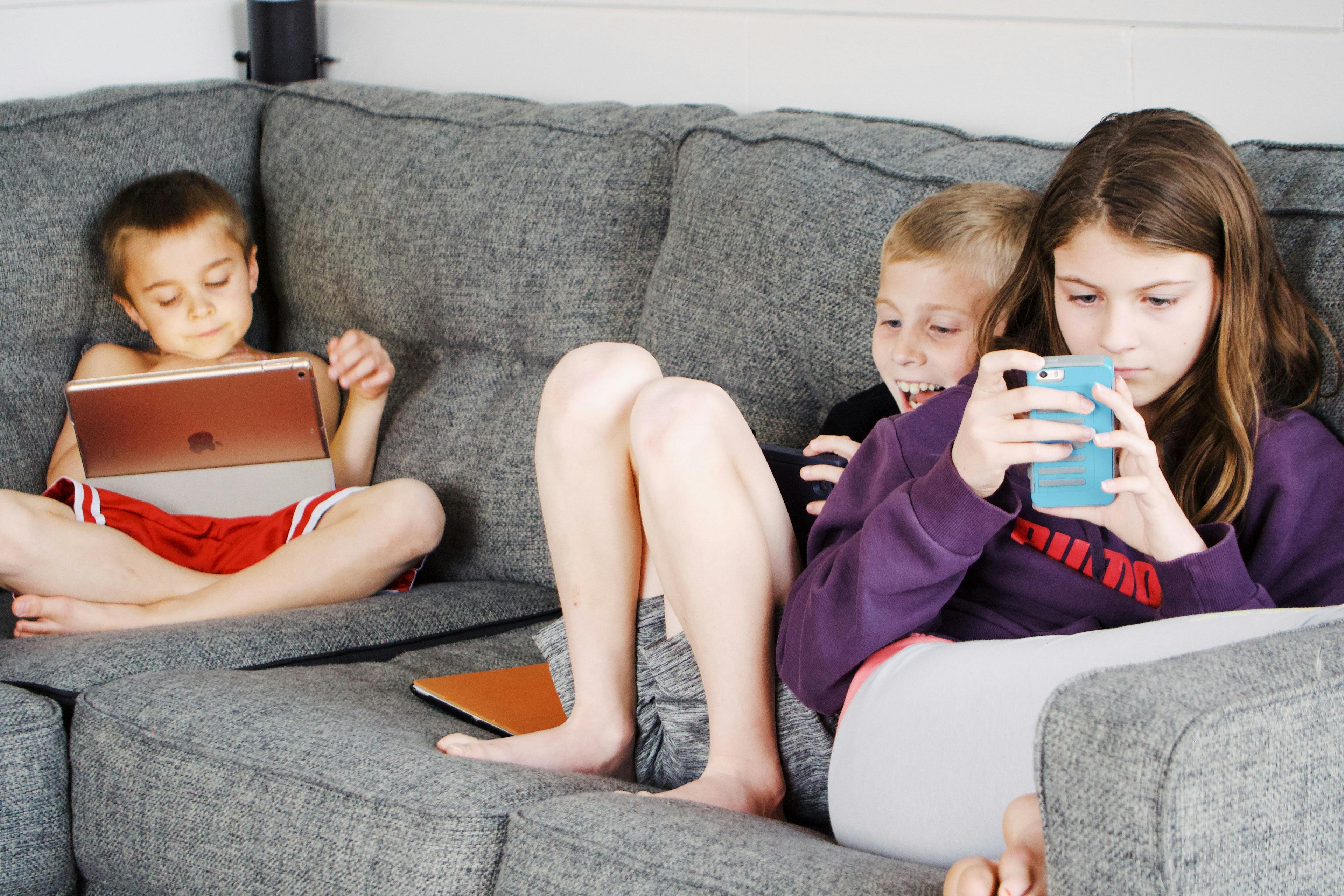 Tre barn som sitter i sofaen med hver sin mobil etter å ha fått beste mobilabonnement for barn.