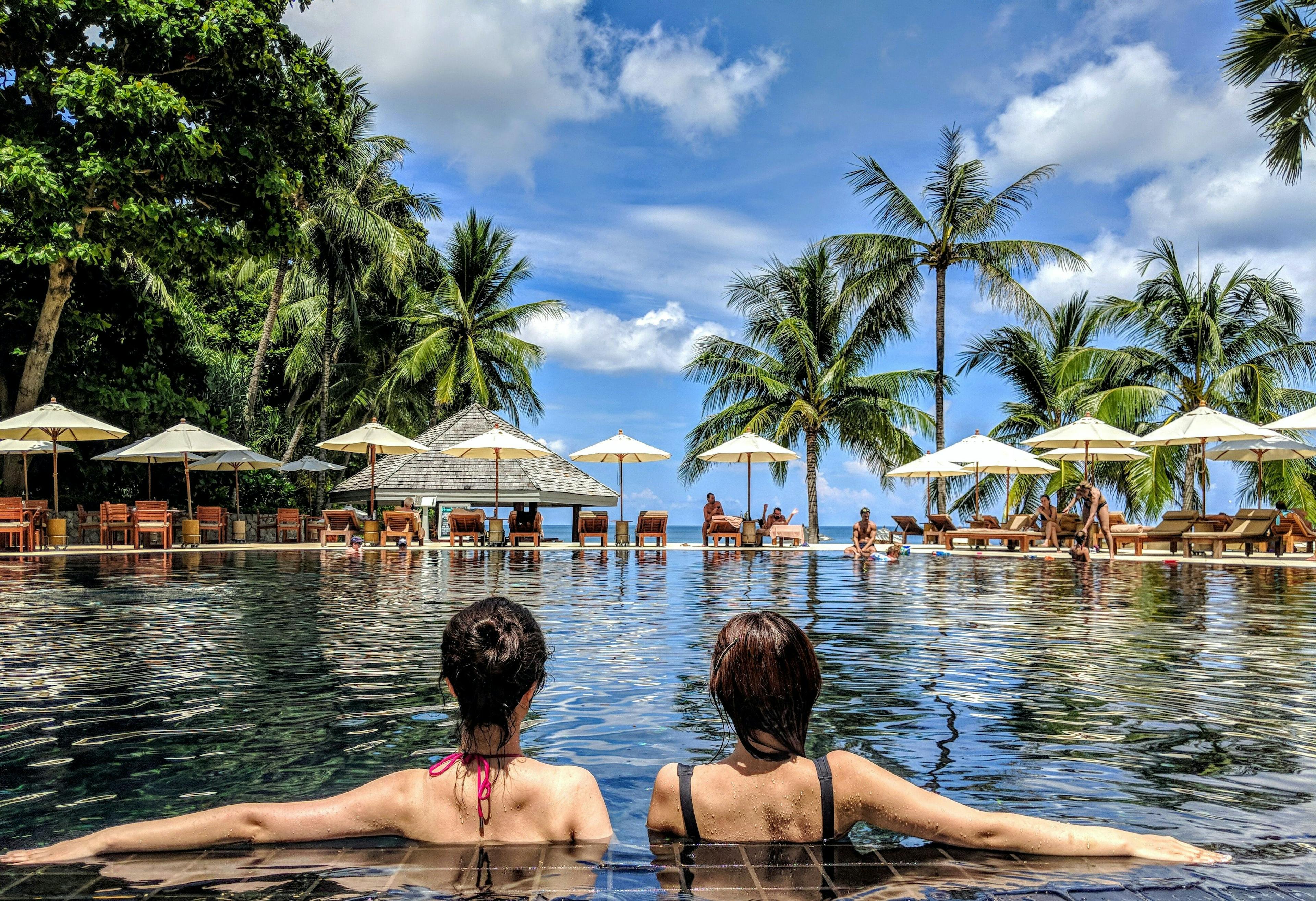 To venninner som bader i et kjempefint basseng på en sydentur de har betalt med beste kredittkort for reise.