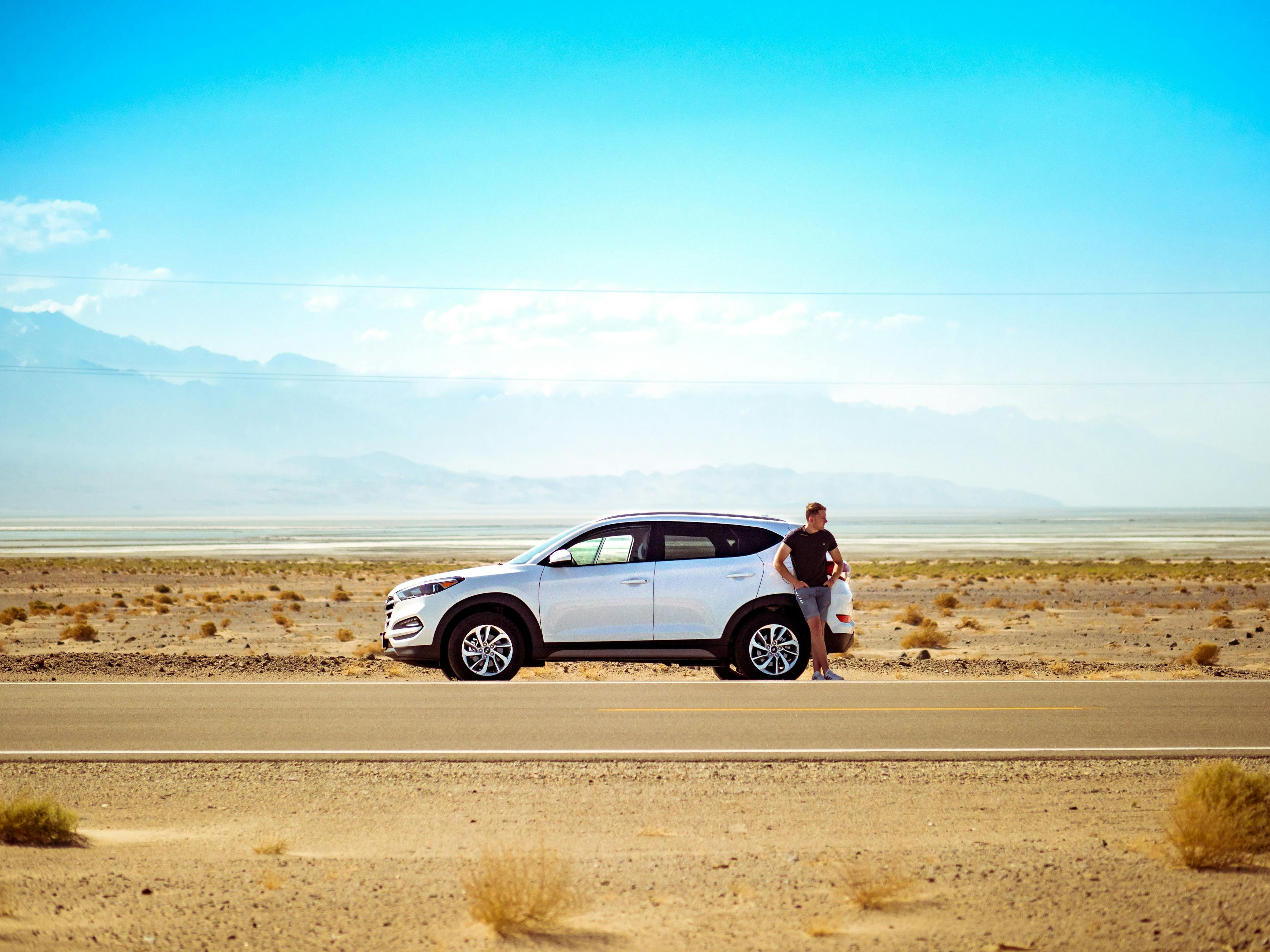 En mann ute i ørkenen med sin hvite bil etter at han tok et fleksibelt forbrukslån.