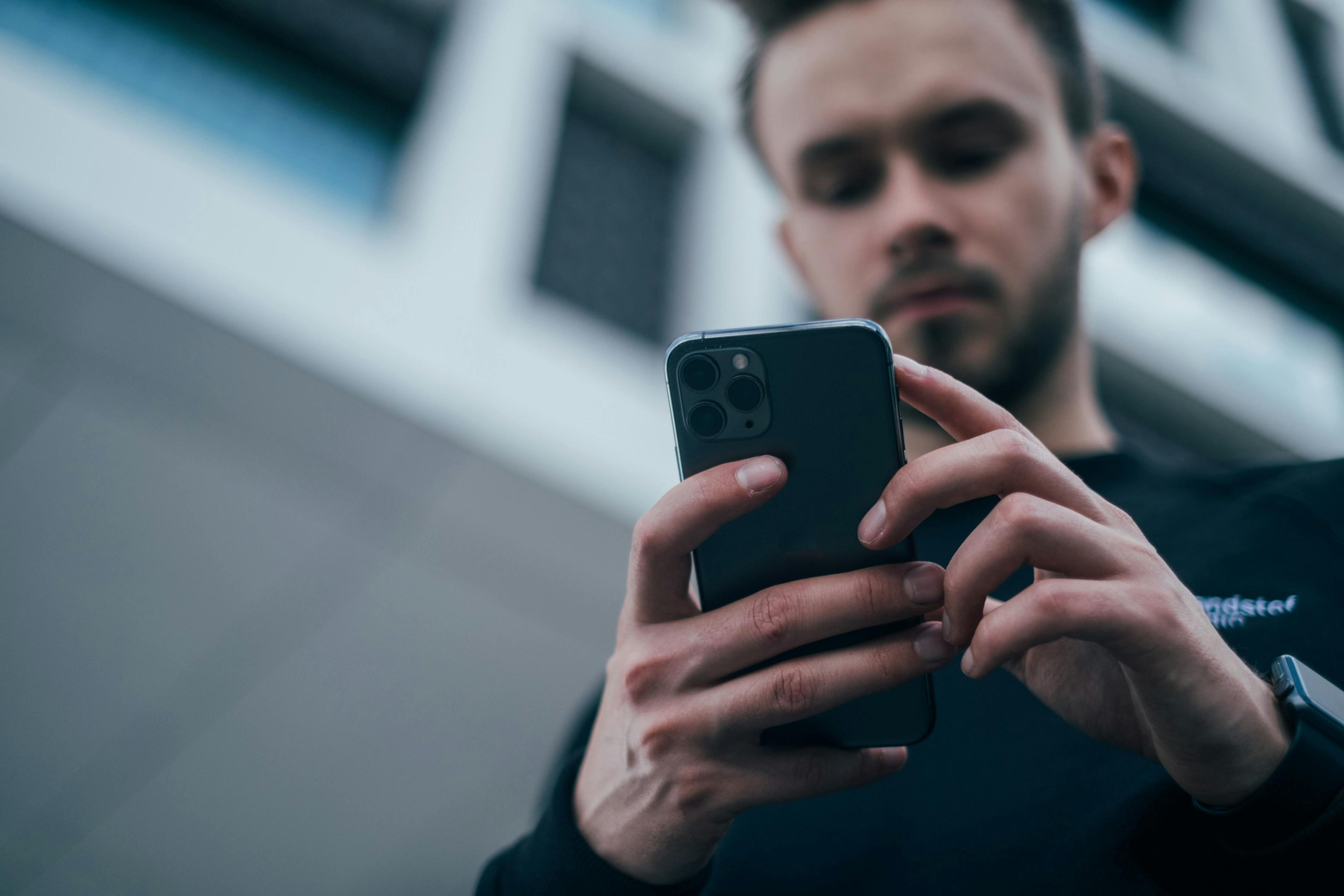 En mann som står med mobilen sin og sammenligner mobilabonnement under 29 år.
