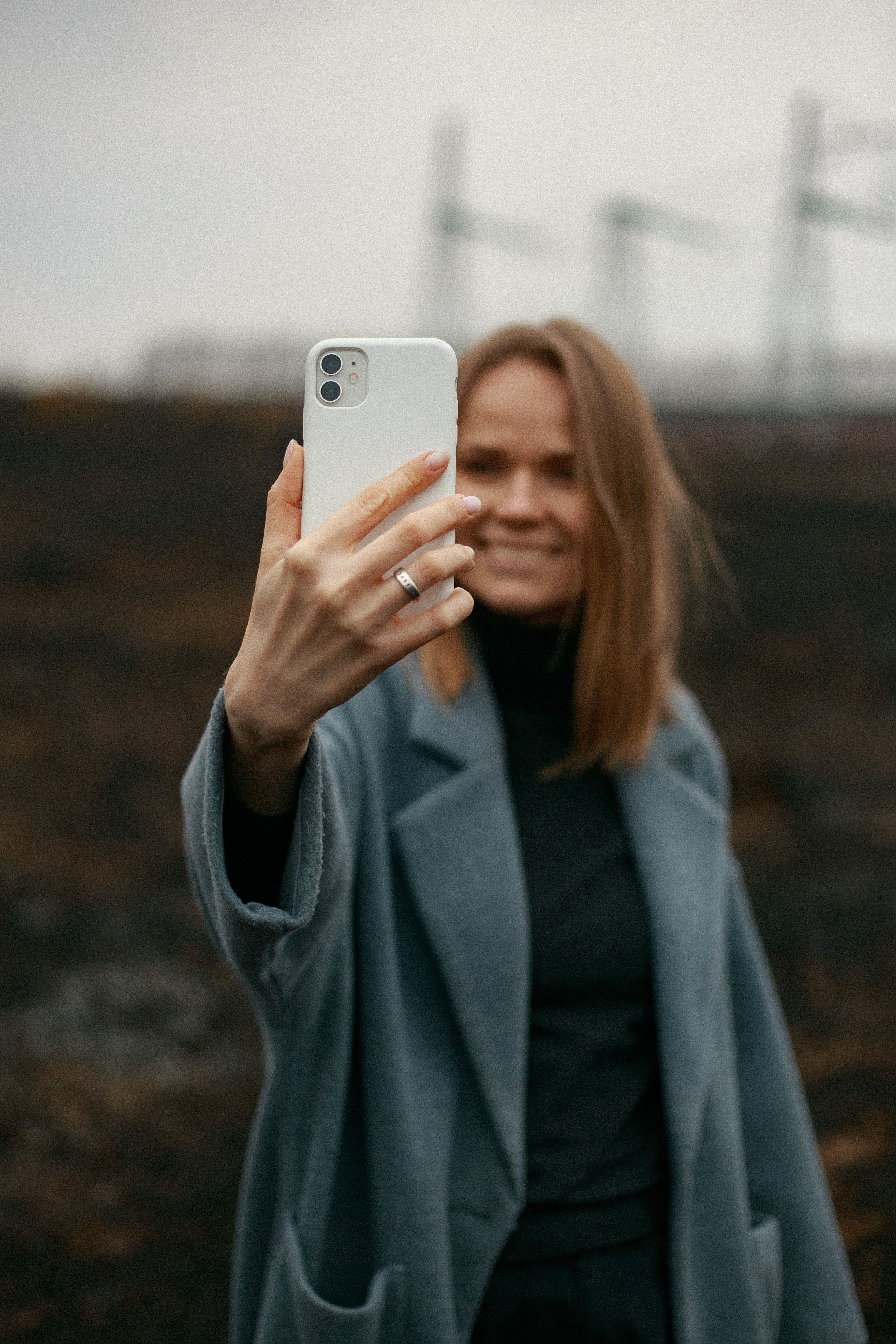 Ei dame som står og tar bilde av seg selv med sin hvite mobiltelefon ute i naturen.
