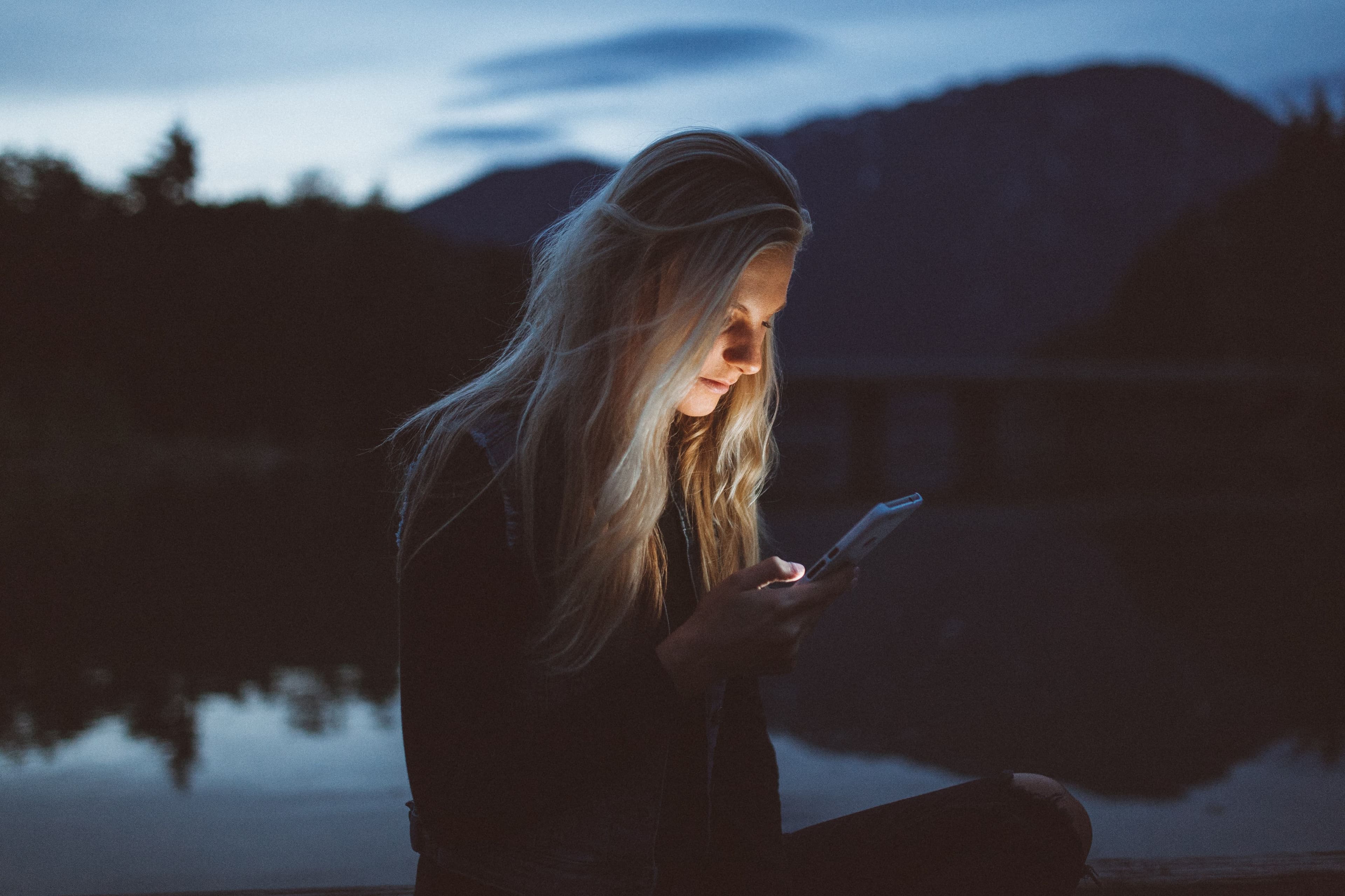Ei dame som sitter med telefonen ute i naturen. Bruker Talkmore mobilabonnement.