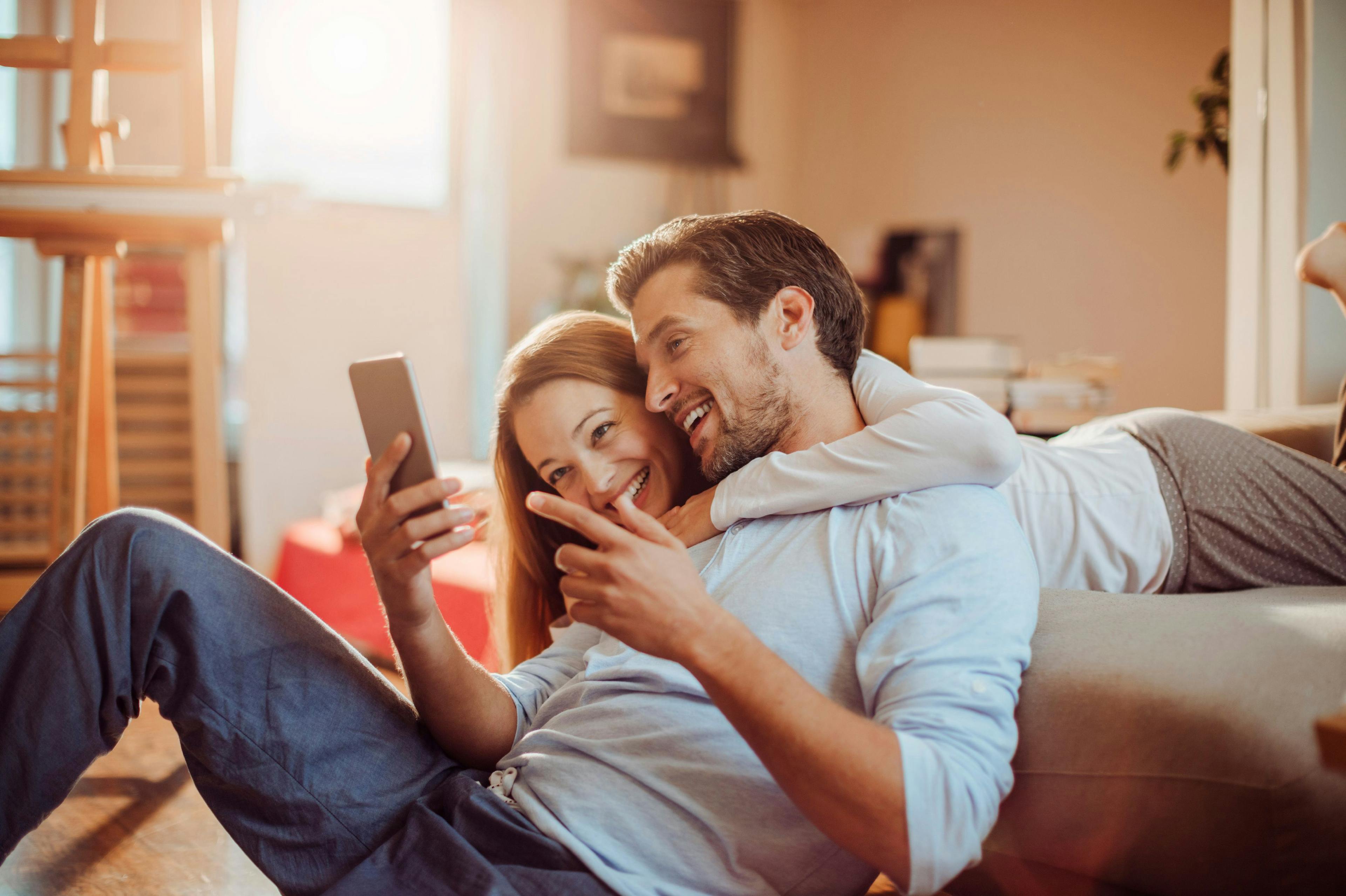 Et lykkelig par som ligger på sofaen og sammenligner forbrukslån så de kan ta det beste lånet.