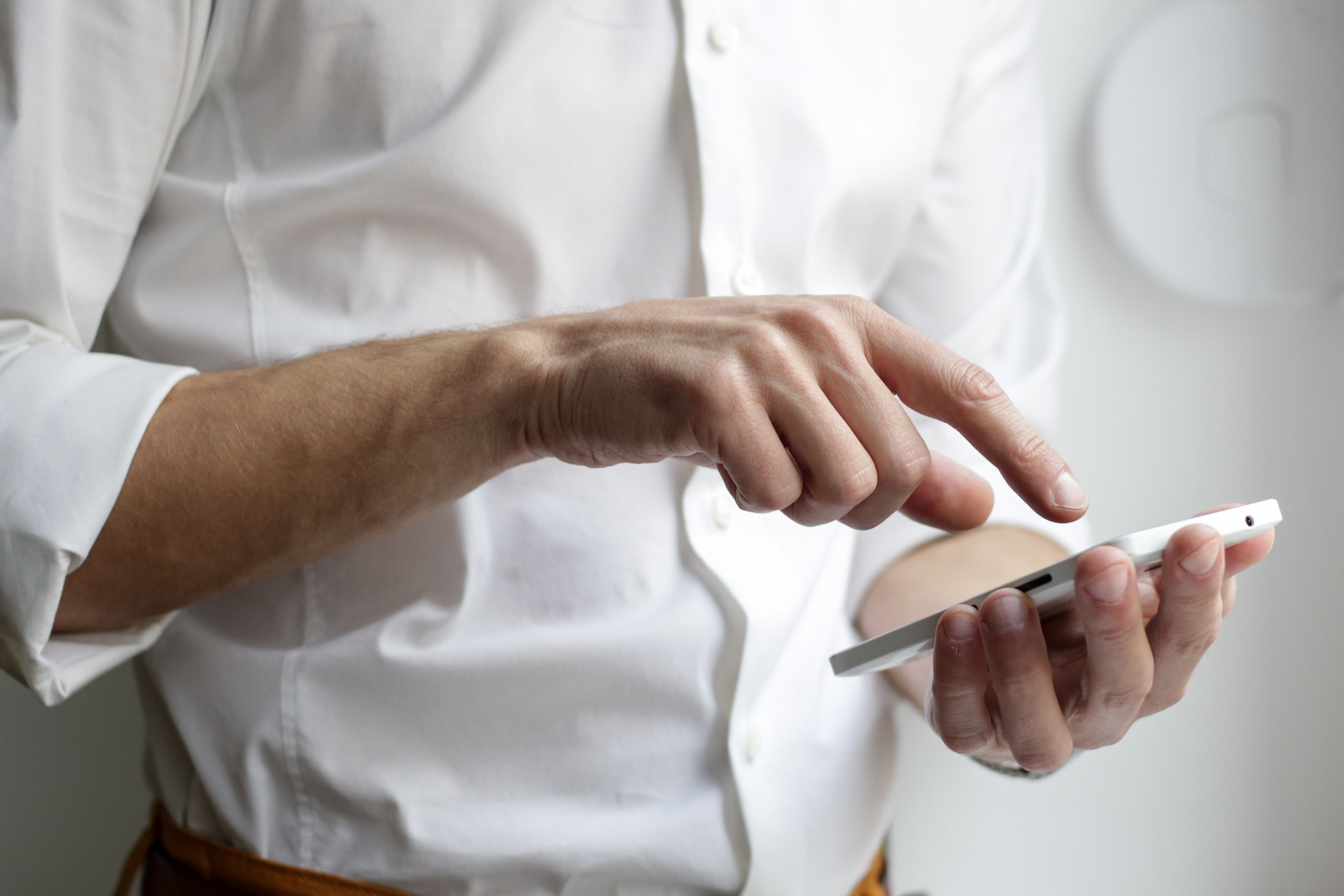 En mann i hvit skjorte som stÄr med mobilen i hÄnden etter at han fikk telefon med forhÄndsbetalt mobilabonnement