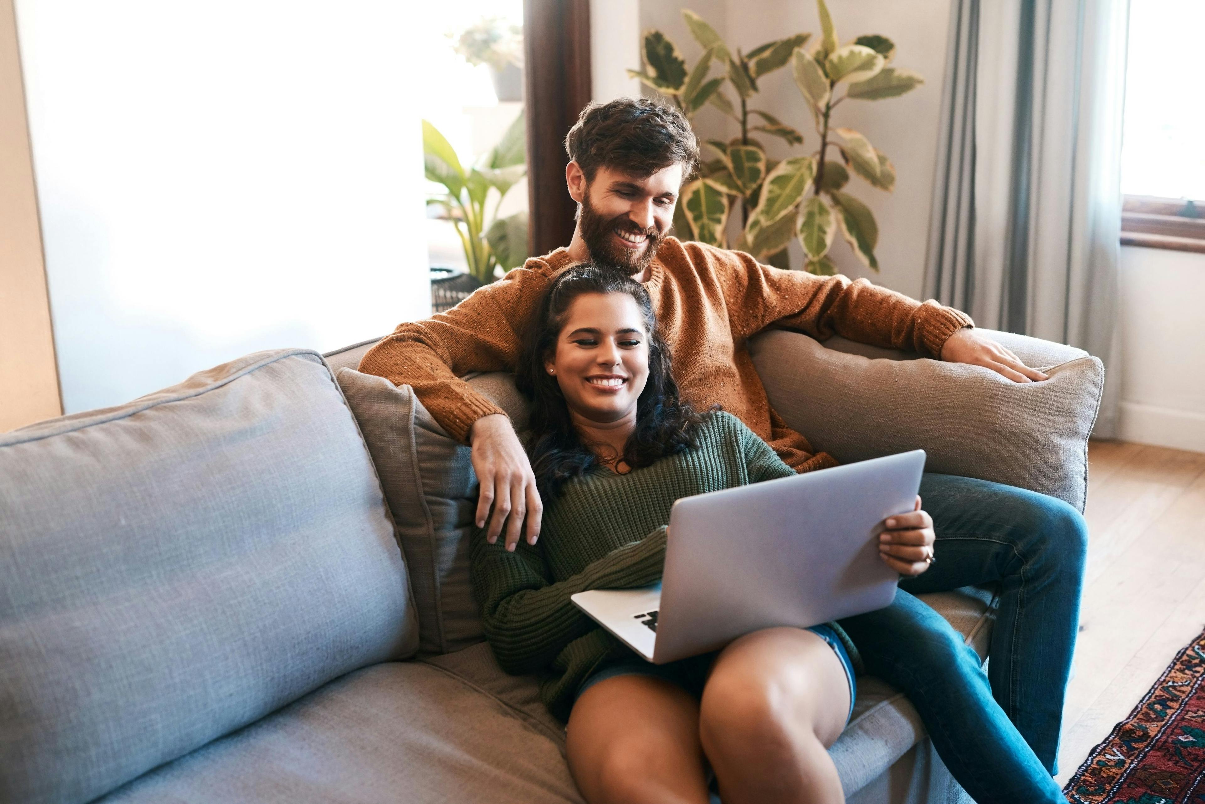 Et yngre kjærestepar som sitter hjemme og er veldig glade fordi de mener at de ikke kan bli påvirket negativt av refinansiering.